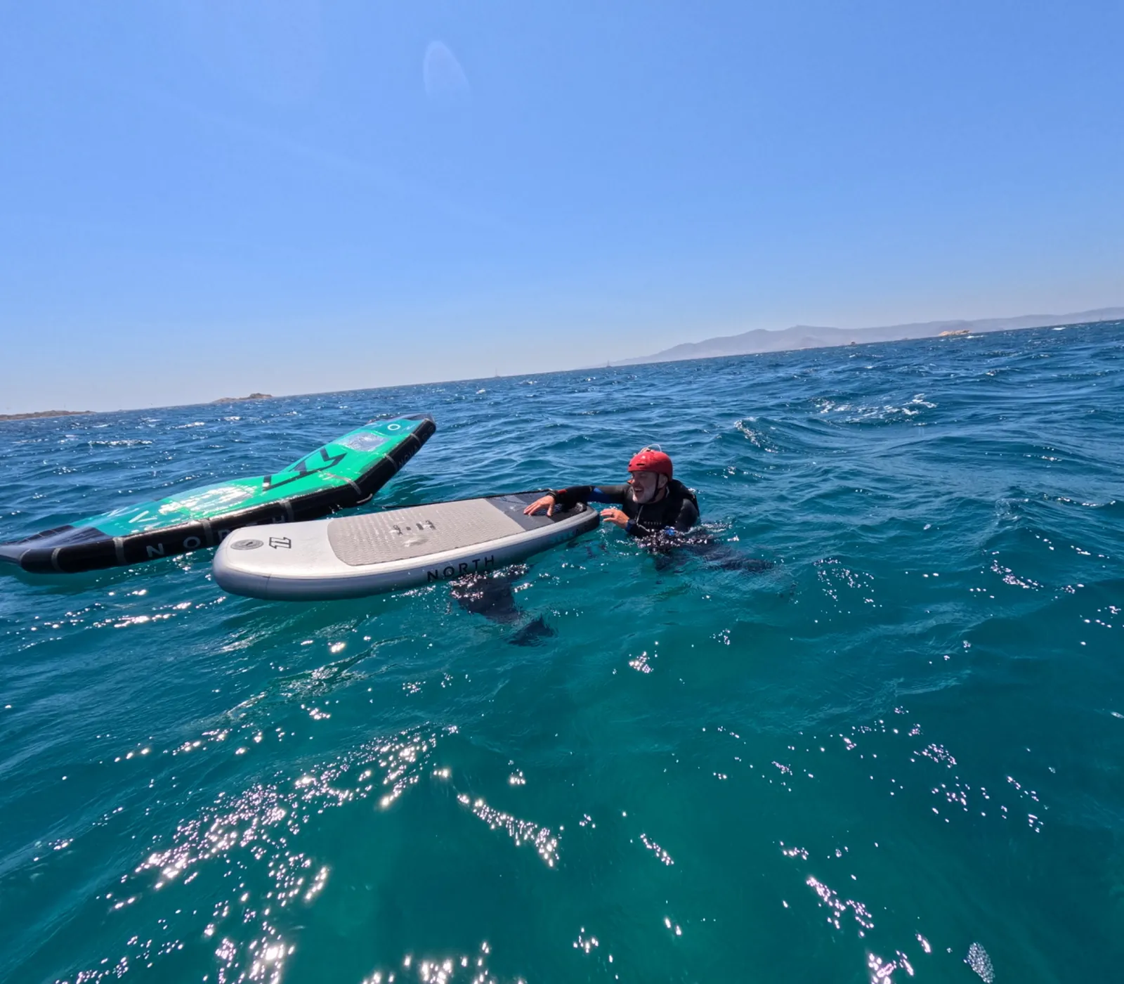 Wing foil student resting beside a board during a training session at sea.