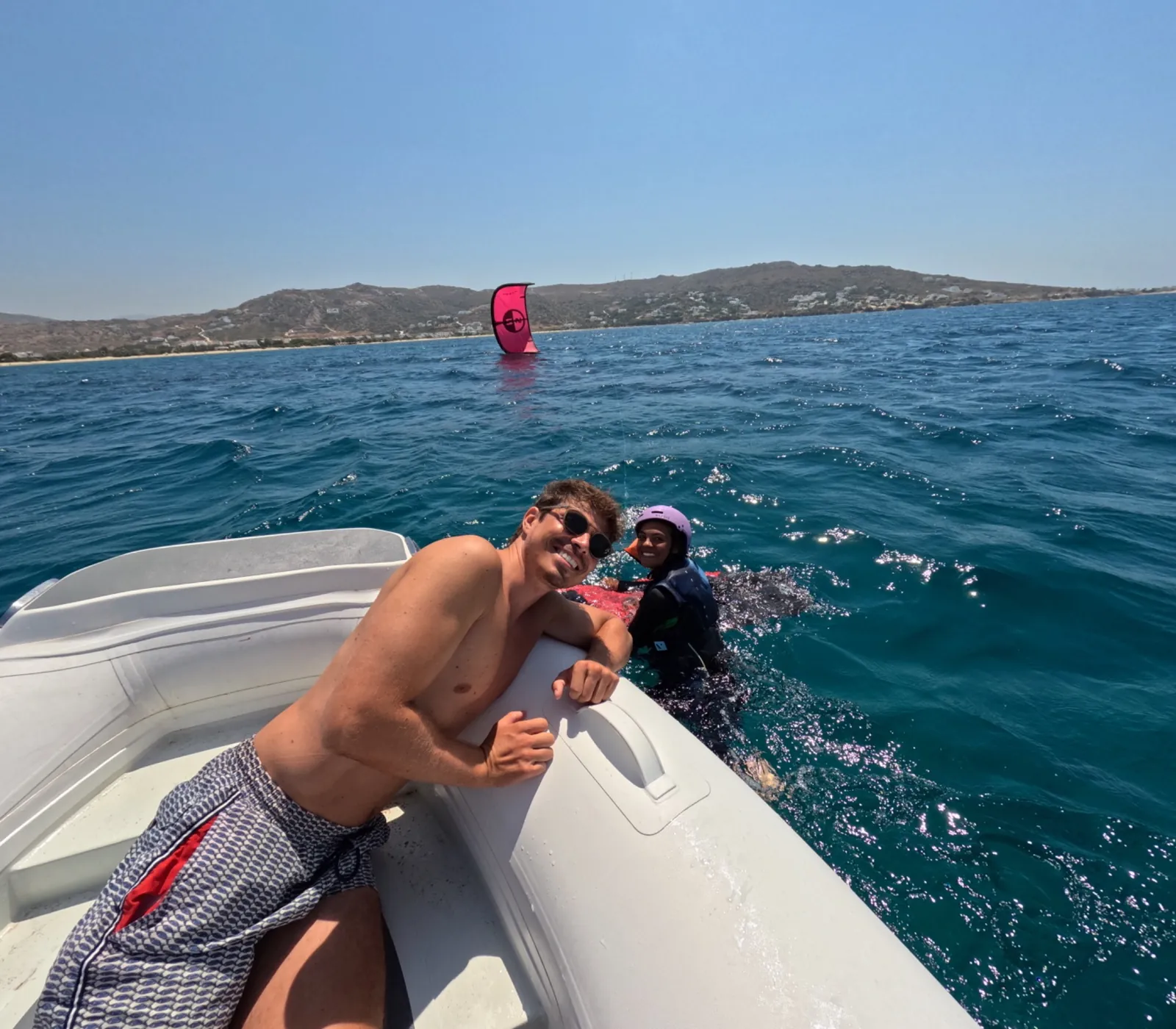 Kitesurfing istructor assisting a student from a support boat during a lesson.
